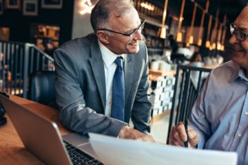 Senior businessman talking with male partner while sitting at a modern coffee shop. Two senior businessman working together on a business report.